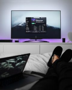 A person lounges with their feet up in front of a flat screen TV
