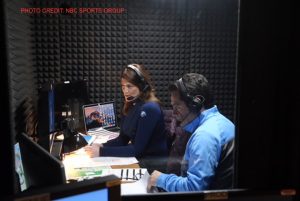 Two people sitting in a recording booth wearing headsets and watching screens.