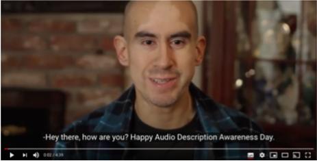 Screenshot of YouTube video: A man with closed caption: "Hey there, how are you? Happy Audio Description Awareness Day."