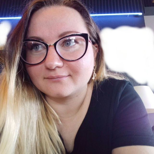 Alicia is a white Slavic woman in her late 30s. She has a round face, long and straight fair hair. Her eyes are grayish-blueish and highlighted by black eyeliner and mascara, no lipstick. She wears music note silver earrings and cat-eye shaped glasses.